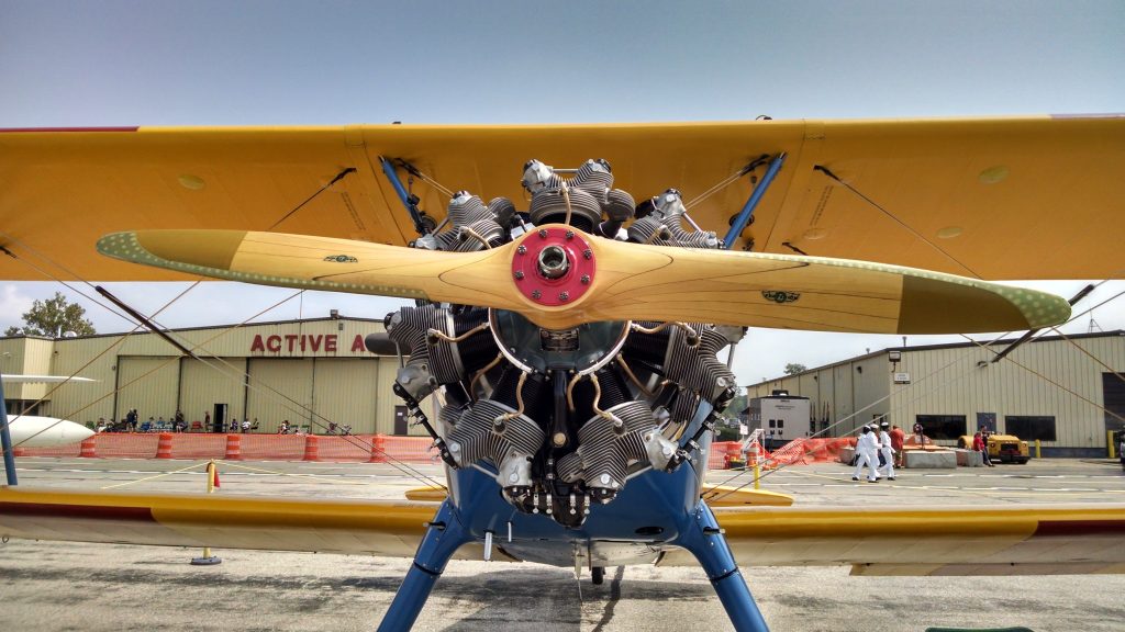 Front view of a vintage Boeing Stearman biplane with yellow wings, a wooden propeller and an intricate radial engine parked on an airfield.