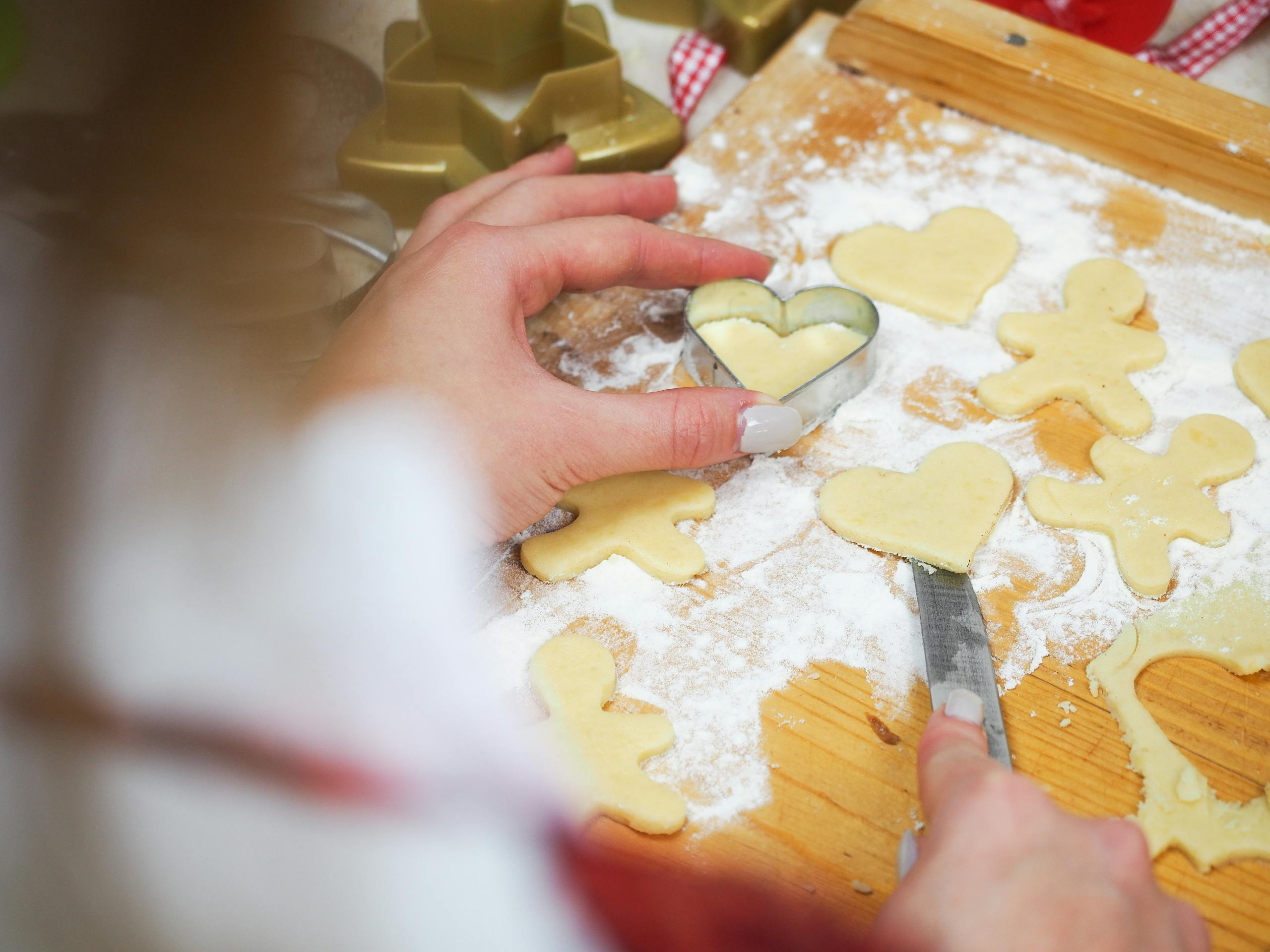 Close-up of hands cutting heart and gingerbread shapes from dough on a floured board.